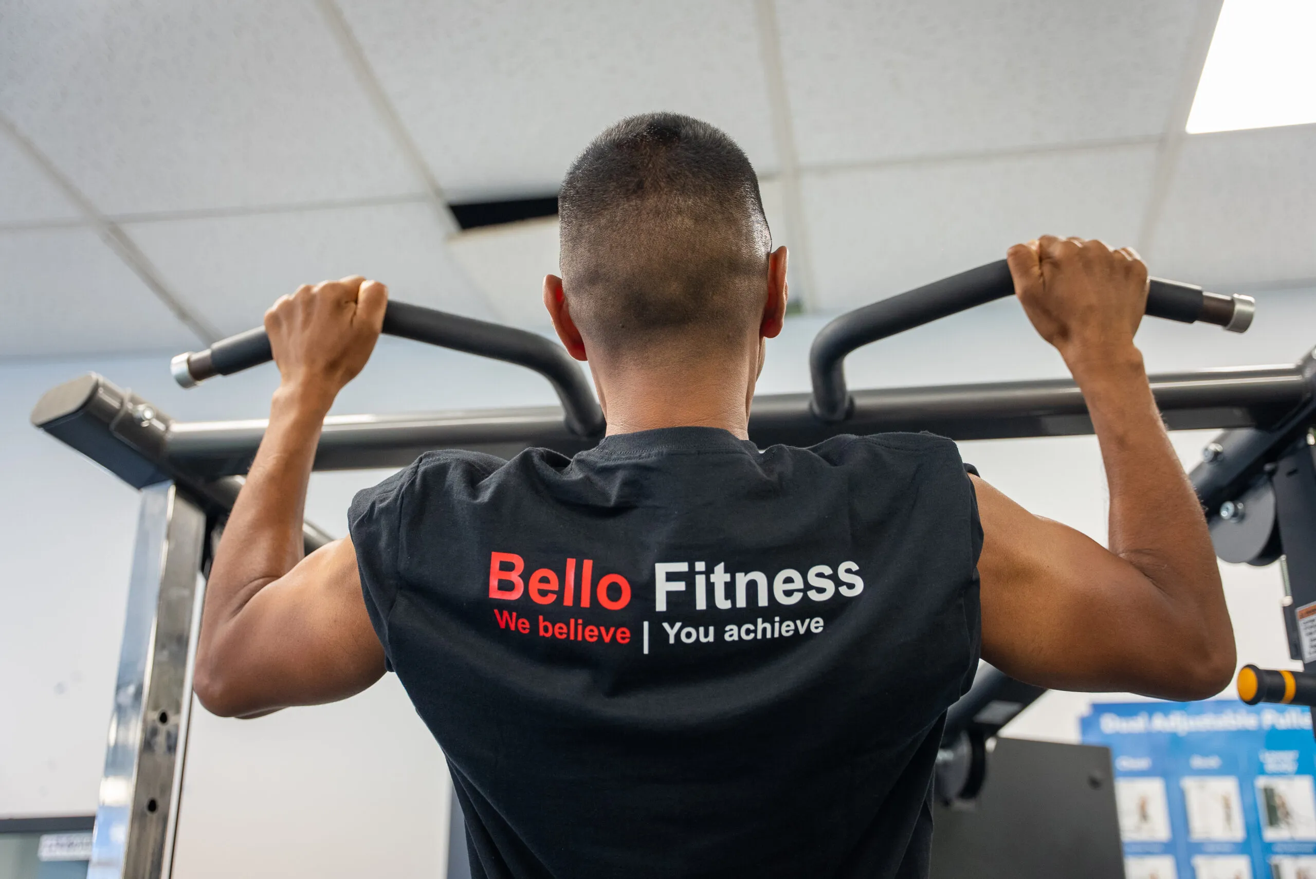 A learner wearing a Bello Fitness shirt at the pull-up bar